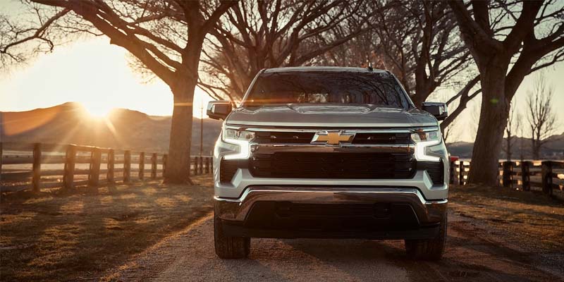 Front of a silver 2023 Chevy Silverado 1500 driving down an open road.